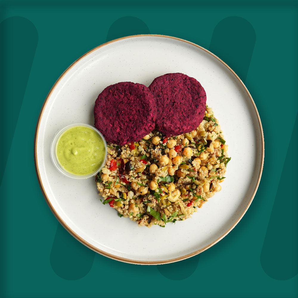 This wholesome dish features two vibrant beetroot patties, packed with earthy flavors and a satisfying texture. Served alongside a colorful quinoa and chickpea salad, mixed with fresh vegetables and herbs for a light yet hearty accompaniment. A side of creamy, tangy green dressing completes the plate, adding a burst of flavor to the dish. Presented on a minimalist plate, the meal sits against a green background, highlighting its fresh and nutrient-rich ingredients