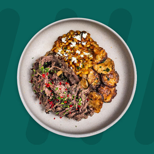  A colorful plate featuring shredded Mexican-spiced chicken garnished with fresh herbs, served alongside a portion of vibrant green cilantro rice. Complementing the dish is a side of roasted corn mixed with crumbled feta cheese, adding a touch of creaminess and texture. The meal is presented on a minimalist ceramic plate with a dark rim, set against a rich green background for a fresh and appetizing presentation. prepped meal.